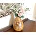 A handmade sunflower vase,  filled with faux daisies and zinnias, decorates a antique buffet table. The vase is made from a dried gourd. 